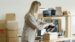 A woman packs sneakers in a box at her e-commerce workspace, surrounded by packing materials.