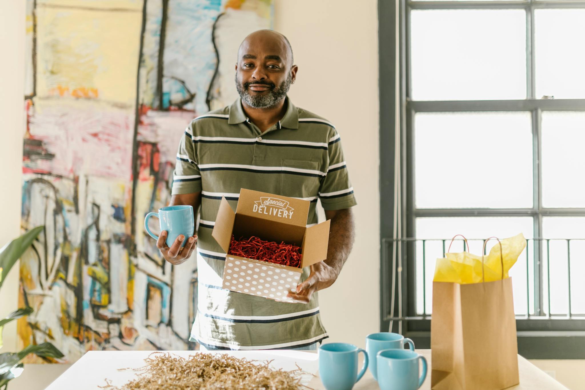 Man packing blue coffee mugs for delivery in a bright, artistic workspace.